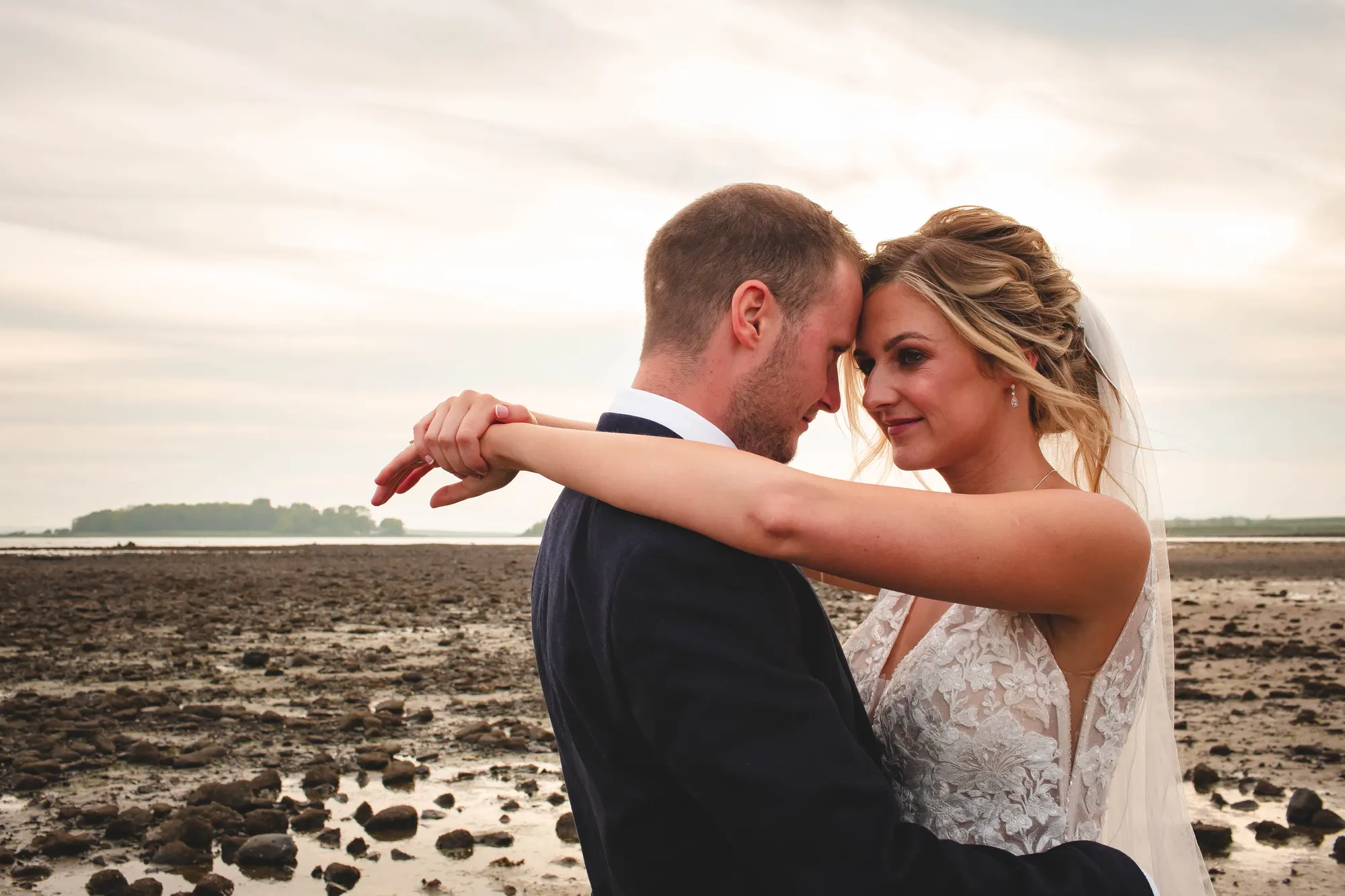 Wedding couple embracing beside the shore at Orange Tree House