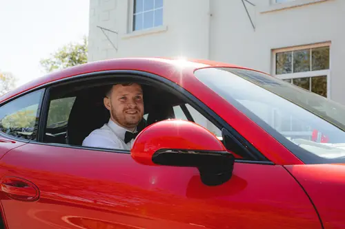 Groom arriving in a red wedding car at Millbrook Lodge on a sunny spring morning in Ballynahinch
