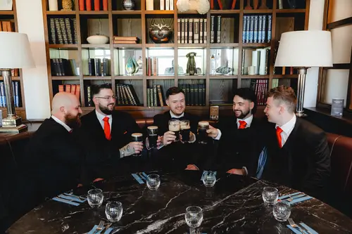 Groom and groomsmen sharing a relaxed drinks toast in the library at Millbrook Lodge, Ballynahinch