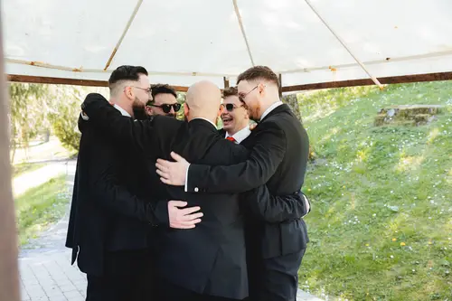 Groom and groomsmen laughing in a group hug under the canopy at Millbrook Lodge, Ballynahinch