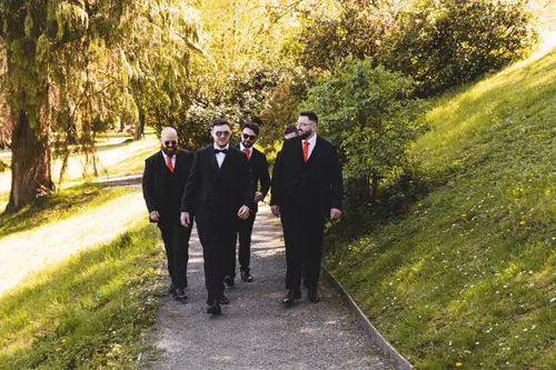 Groom and groomsmen in black tie walking along a sunlit path at Millbrook Lodge, Ballynahinch