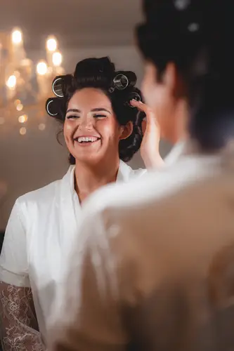 Bride laughing in hair rollers and robe during wedding morning prep at Millbrook Lodge, Ballynahinch