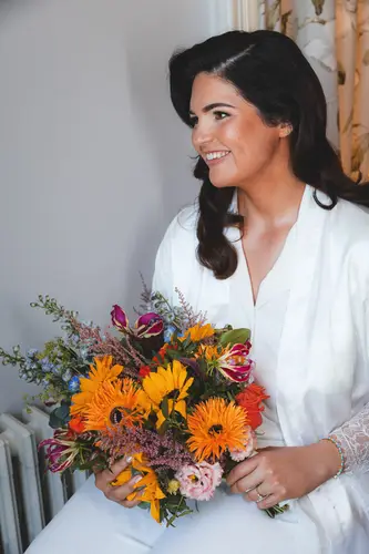 Bride in a white robe smiling with her spring bouquet during wedding morning prep at Millbrook Lodge