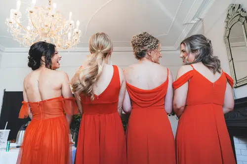 Bridesmaids in orange dresses laughing together while getting ready at Millbrook Lodge in Ballynahinch