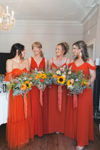 Bridesmaids in red dresses laughing with bouquets during morning prep at Millbrook Lodge