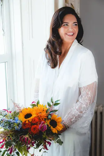 Bride smiling in a bridal robe with sunflower bouquet during morning prep at Millbrook Lodge