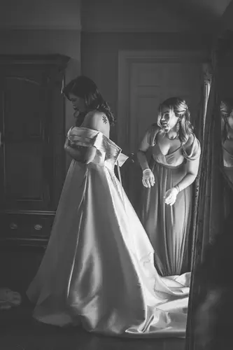 Black and white bridal prep as a bridesmaid helps fit the wedding dress by window light at Millbrook Lodge
