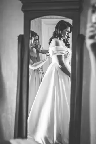 Black and white bridal prep at Millbrook Lodge as a bridesmaid fastens the bride’s wedding dress in the mirror.