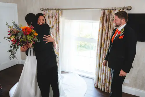 Emotional wedding morning hug by the window at Millbrook Lodge, with the bride holding her bouquet