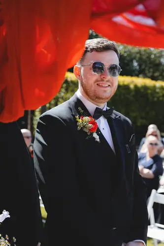 Groom in sunglasses and a black tuxedo during the sunny outdoor ceremony at Millbrook Lodge, Ballynahinch
