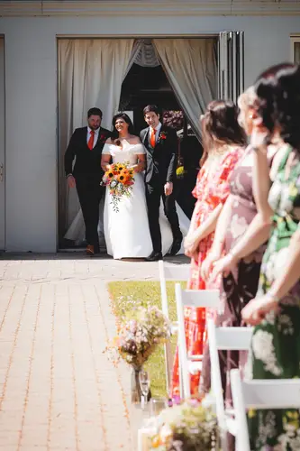 Bride walking down the outdoor aisle at Millbrook Lodge in Ballynahinch, with guests smiling in the spring sunshine