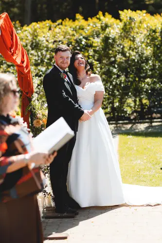 Bride and groom laughing during outdoor vows in the sunny garden ceremony at Millbrook Lodge, Ballynahinch