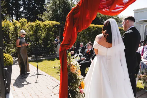 Couple exchanging vows under a red canopy during an outdoor ceremony at Millbrook Lodge, Ballynahinch