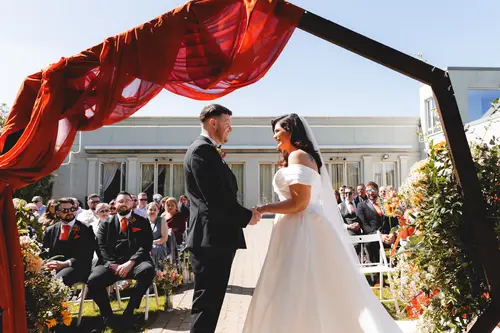 Couple exchanging vows beneath the ceremony arch in sunny gardens at Millbrook Lodge, Ballynahinch