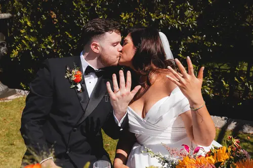 Bride and groom share their first kiss during a sunny outdoor ceremony at Millbrook Lodge, Ballynahinch