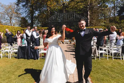 Bride and groom walking back up the aisle as guests applaud at Millbrook Lodge, Ballynahinch