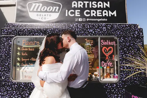 Bride and groom share a kiss beside the ice cream truck at Millbrook Lodge in sunny Ballynahinch