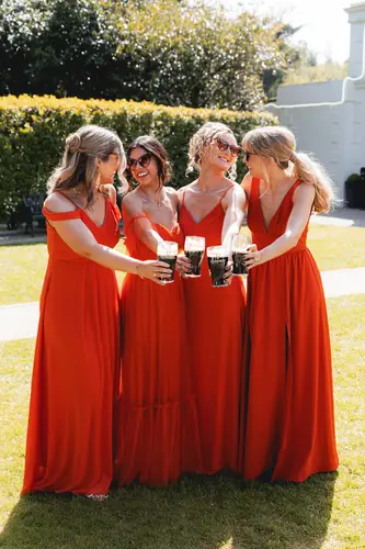 Bridesmaids in red dresses laughing over drinks in the sunshine at Millbrook Lodge, Ballynahinch