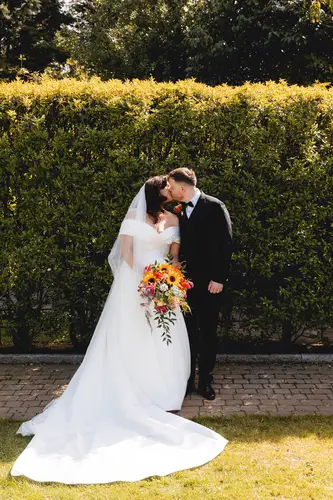 Bride and groom share a sunlit kiss beside the gardens at Millbrook Lodge, Ballynahinch
