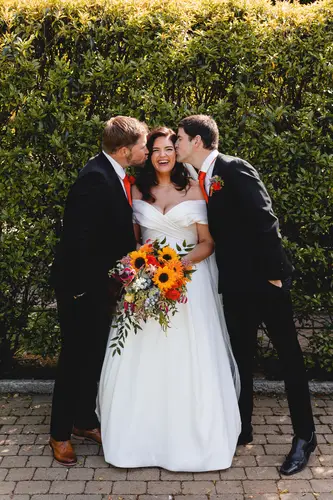Bride laughing as the bridal party give cheek kisses in the sunny gardens at Millbrook Lodge