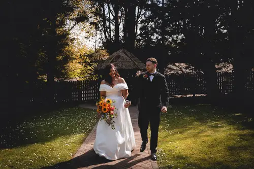 Bride and groom walking along the garden path at Millbrook Lodge in warm evening light
