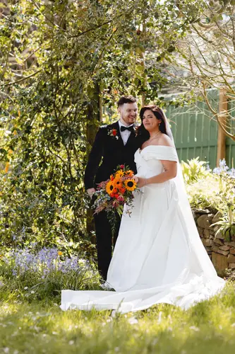 Bride and groom in sunlit garden portraits at Millbrook Lodge, Ballynahinch, with the bouquet in hand