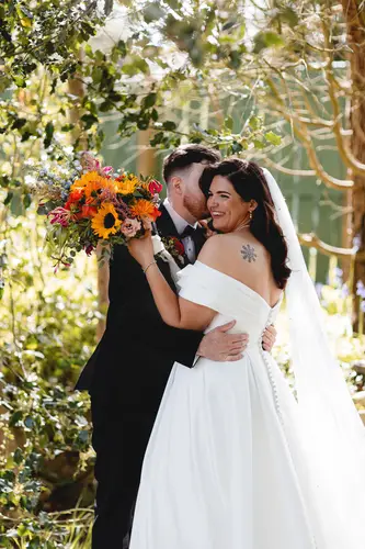 Bride and groom share a quiet garden portrait at Millbrook Lodge, Ballynahinch, with a sunflower bouquet in soft spring light
