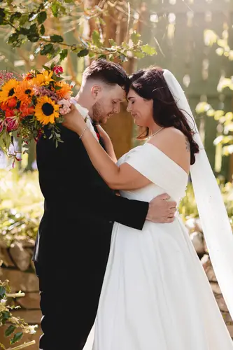 Bride and groom embracing in soft woodland light at Millbrook Lodge, with a sunflower bouquet and flowing veil