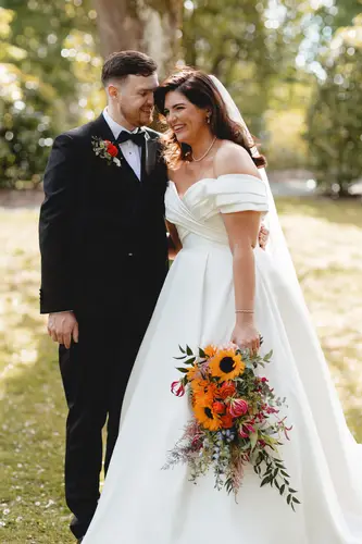 Newlyweds share a golden-hour portrait in the gardens at Millbrook Lodge, with a sunflower bouquet in hand