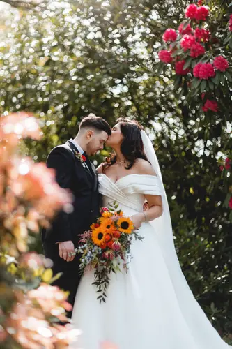 Bride and groom share a quiet kiss in the gardens at Millbrook Lodge, Ballynahinch, with a sunflower bouquet in soft spring light
