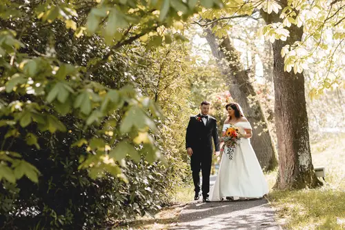 Bride and groom walking along a dappled woodland path at Millbrook Lodge in Ballynahinch