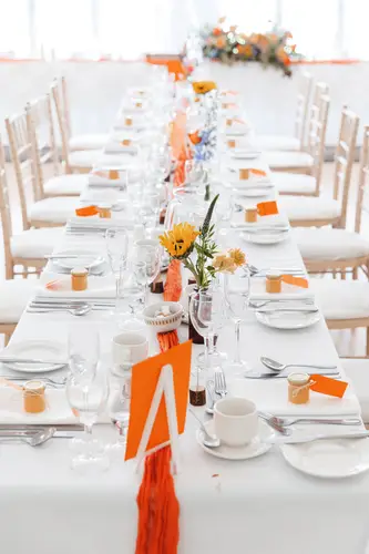 Reception tables at Millbrook Lodge in Ballynahinch with floral centrepieces, place cards and warm orange accents
