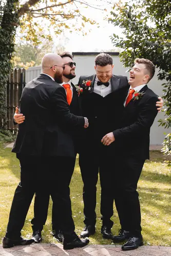 Groomsmen laughing in the gardens at Millbrook Lodge, Ballynahinch, in black suits with spring buttonholes