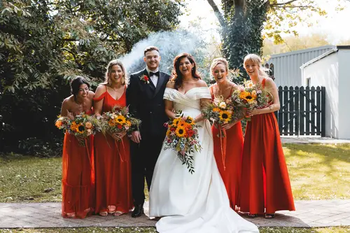 Bride, groom and bridesmaids in red dresses enjoying sunny garden portraits at Millbrook Lodge, Ballynahinch