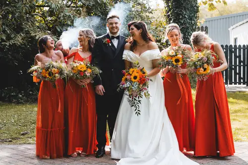 Bride, groom and bridesmaids in orange dresses during sunny outdoor portraits at Millbrook Lodge