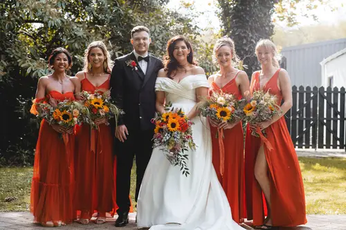 Bridal party portrait in the sunlit gardens at Millbrook Lodge, Ballynahinch, with orange bridesmaid dresses and spring bouquets
