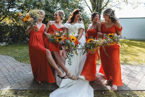 Bride laughing with bridesmaids in orange dresses during sunny garden portraits at Millbrook Lodge