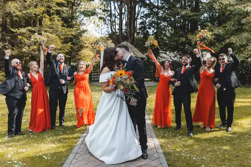 Newlyweds kiss among their bridal party in the woodland garden at Millbrook Lodge, Ballynahinch