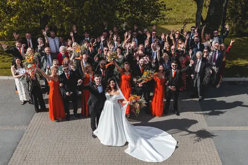 High angle group portrait of the couple, bridal party and guests waving outside Millbrook Lodge in sunny Ballynahinch