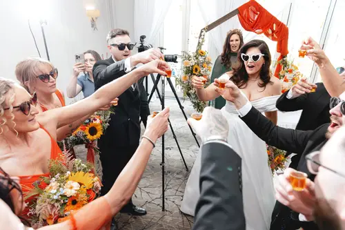 Wedding guests in sunglasses toast shots with the couple during a bright Millbrook Lodge reception party