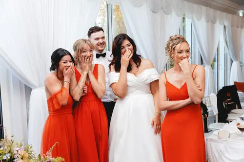 Bride and bridesmaids in red dresses laughing during the Millbrook Lodge wedding reception