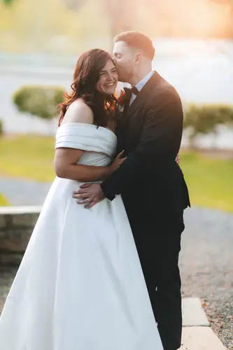 Bride and groom share a warm lakeside embrace during golden hour at Millbrook Lodge, Ballynahinch