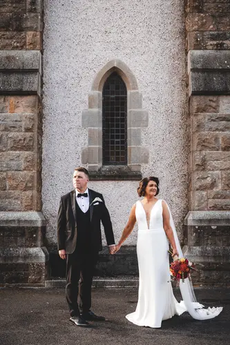 Bride and groom holding hands by an arched stone window at Cavan Crystal in Cavan