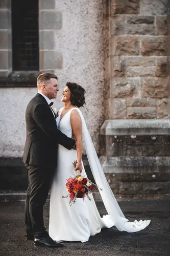 Bride and groom portrait by a stone wall at Cavan Crystal in Cavan, with soft natural light and a bridal bouquet