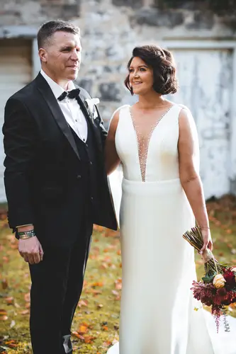 Bride and groom in an outdoor couple portrait by a stone wall at Cavan Crystal, County Cavan, with autumn light and bouquet