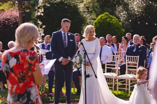 Bride and groom share vows during an outdoor ceremony at Old Rectory, Killyman, with guests watching in sunny garden light