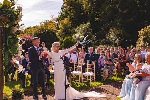 Bride and groom exit their outdoor ceremony at Old Rectory in Killyman as guests cheer in the sunlit garden