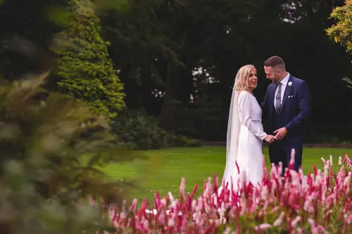 Bride and groom holding hands in the gardens at Old Rectory, Killyman, framed by soft floral foreground