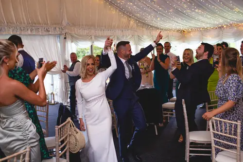 Couple entering their marquee reception at Old Rectory, Killyman, as guests cheer beneath warm fairy lights