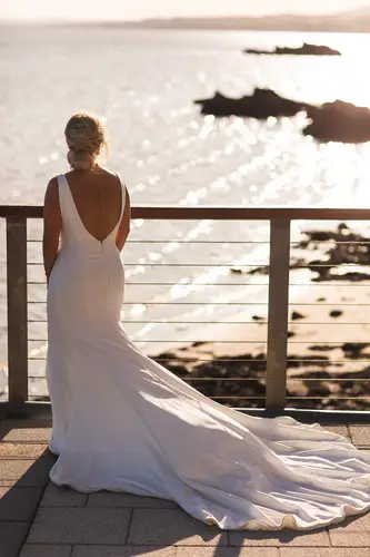 Bride on a balcony at Redcastle Hotel in Moville, backlit at golden hour with a sea view and flowing wedding dress